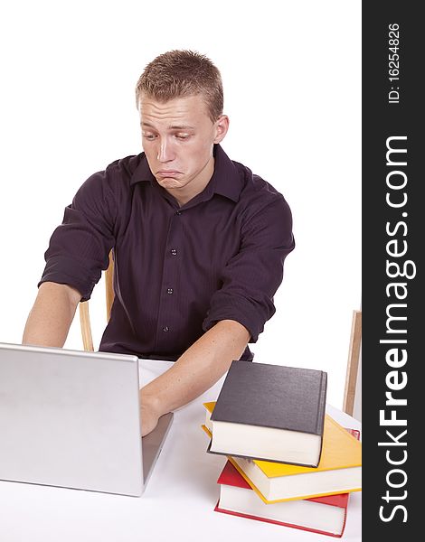 A young man sitting and working on his laptop with a stack of books with a sad expression on his face. A young man sitting and working on his laptop with a stack of books with a sad expression on his face.