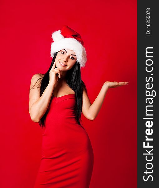 Beautiful brunette girl wearing a Santa's hat standing with her hand up, place your product here