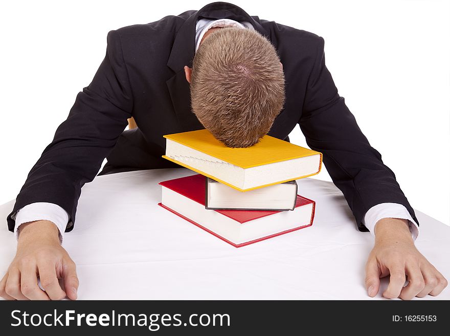 A young business man sitting at a table with his head on a stack of books giving up. A young business man sitting at a table with his head on a stack of books giving up.