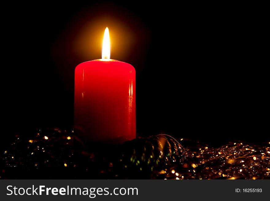 Burning candle with a glass toy in a tinsel on a black background. Burning candle with a glass toy in a tinsel on a black background