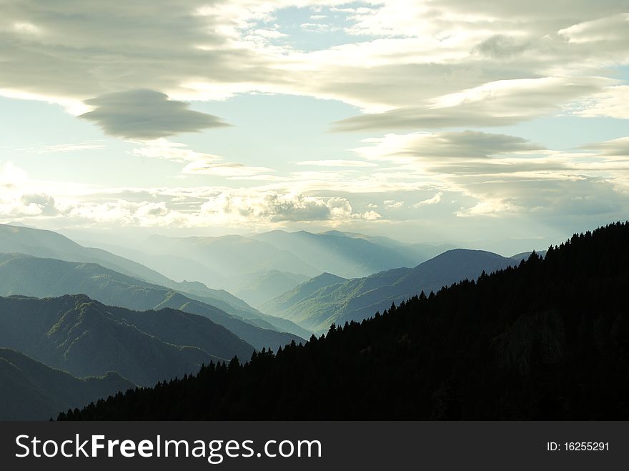 Mountain peeks and dark forest with a blue cloudy sky. Mountain peeks and dark forest with a blue cloudy sky
