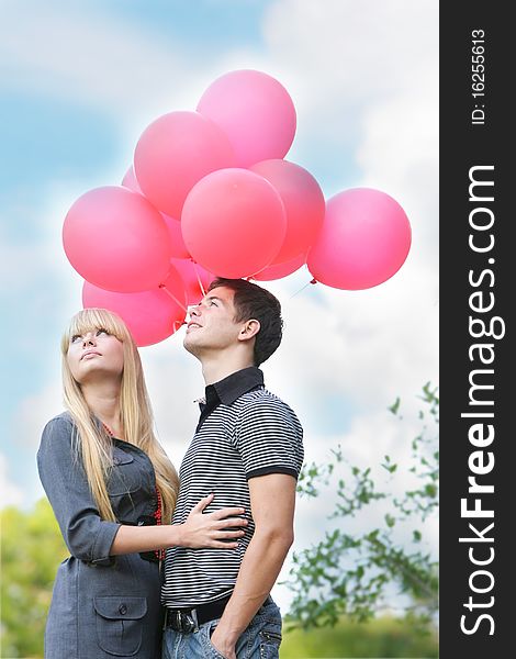 Young loving couple with red balloons on natural background