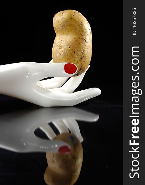 Potato in the white hand with reflection. Black background. Potato in the white hand with reflection. Black background