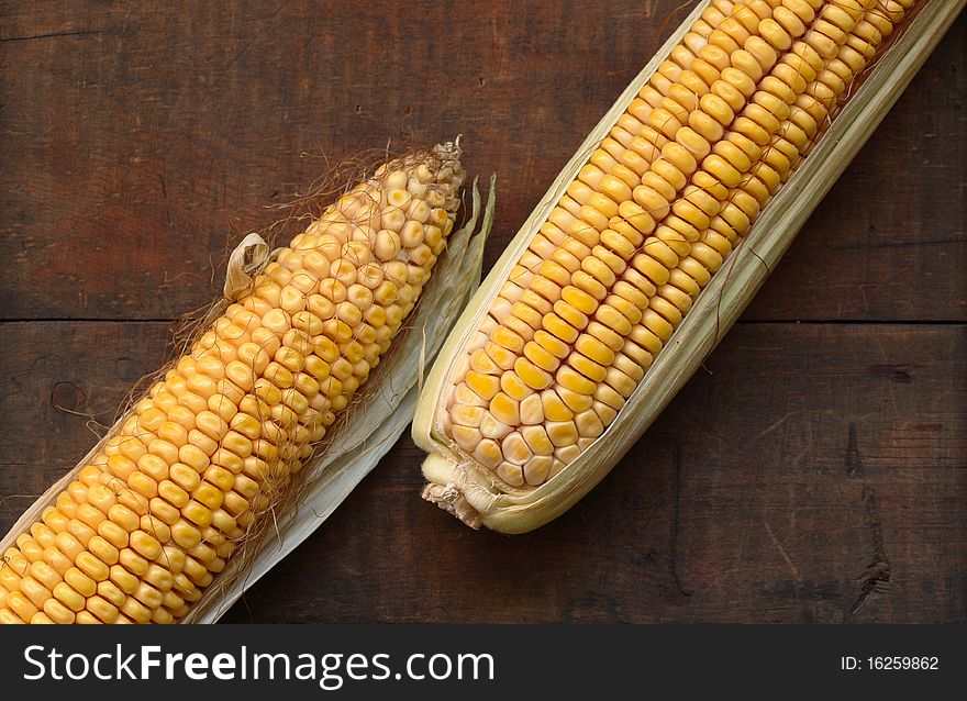 Two raw corncobs lying on wooden background. Two raw corncobs lying on wooden background