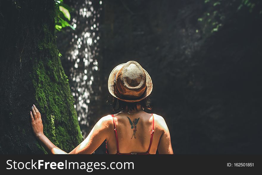 Young woman tourist with straw hat deep in the rainforest with waterfall background. Bali island. Indonesia.