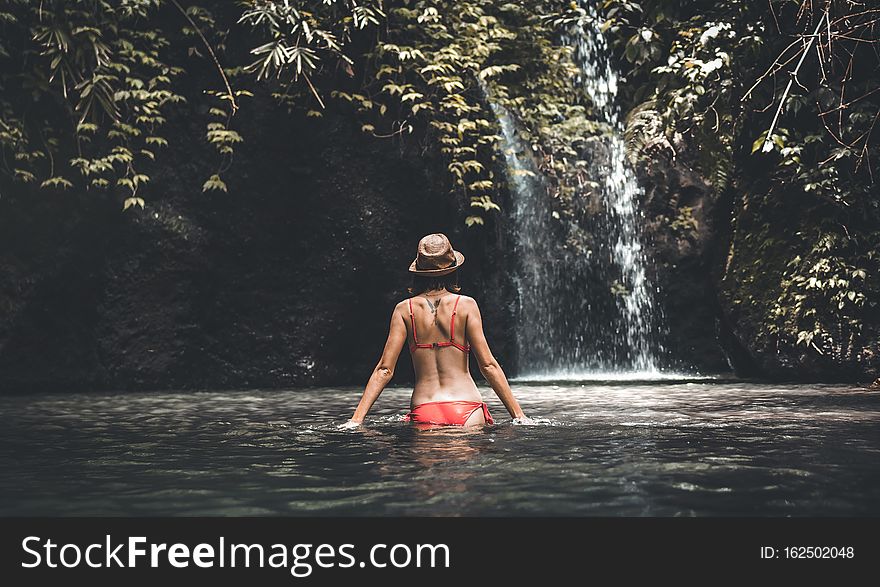 Rear view of Young woman tourist with straw hat in the deep jungle with waterfall. Real adventure concept. Bali island.