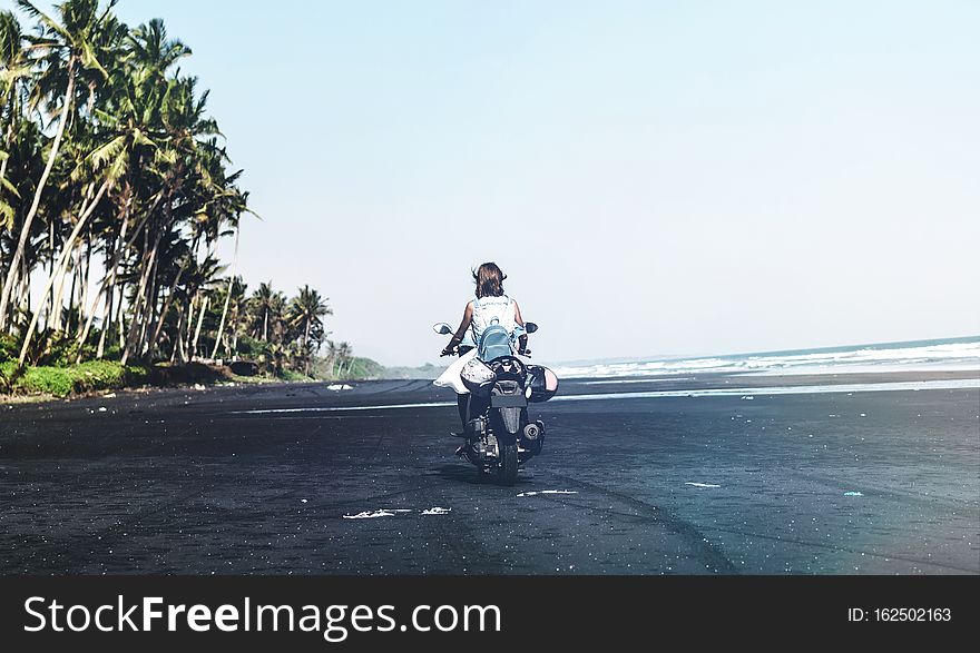 Young Woman Driving A Scooter At The Beach With Black Sand. Bali Island.