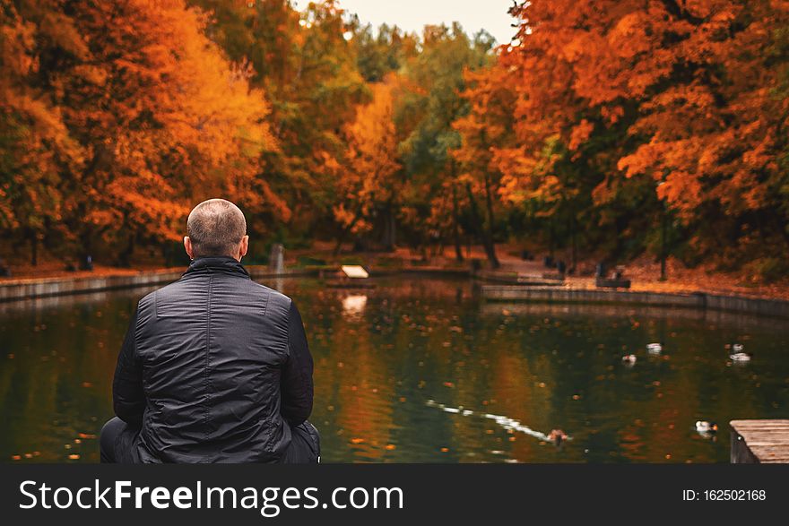 Alone man sits beside a pond in the park. Autumn background.