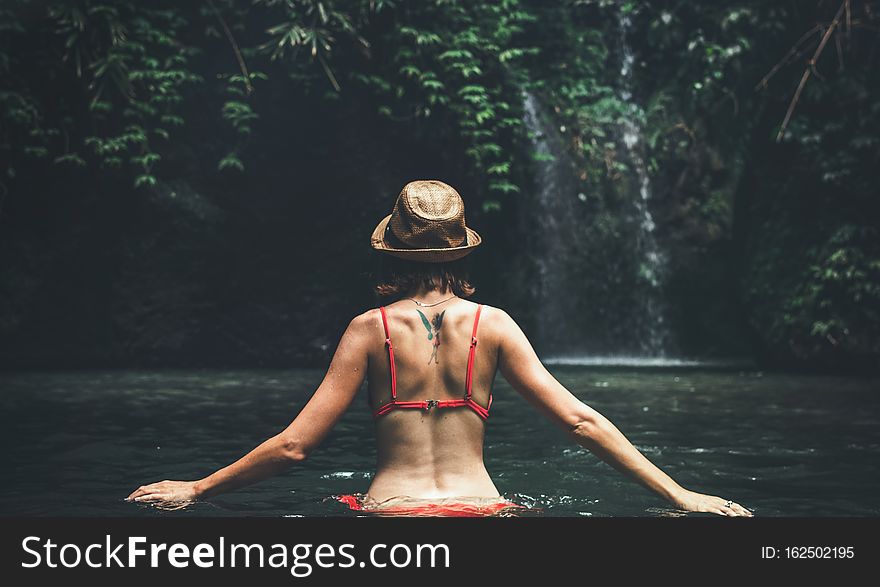 Young Woman Tourist With Straw Hat In The Deep Jungle With Waterfall. Real Adventure Concept. Bali Island.
