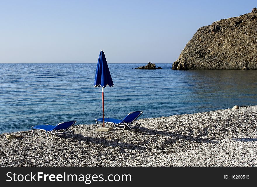 Solitary beach with one blue umbrella and 2 beach beds