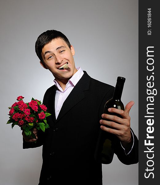 Handsome romantic young man holding rose flower and vine bottle prepared for a date. gray background