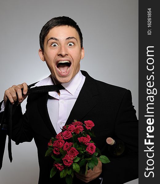 Handsome romantic young man holding rose flower and vine bottle prepared for a date. gray background