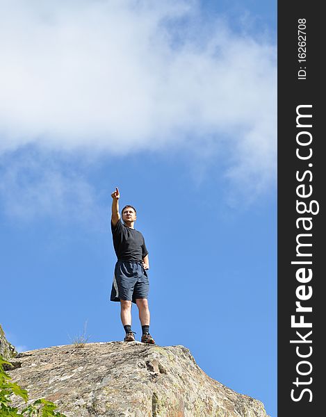 A young man stands on a cliff top and shows the direction of a finger, a blue sky background