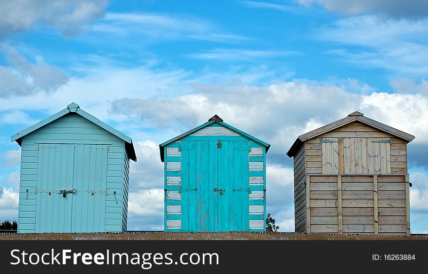 Three beach huts against a cloudy blue sky
