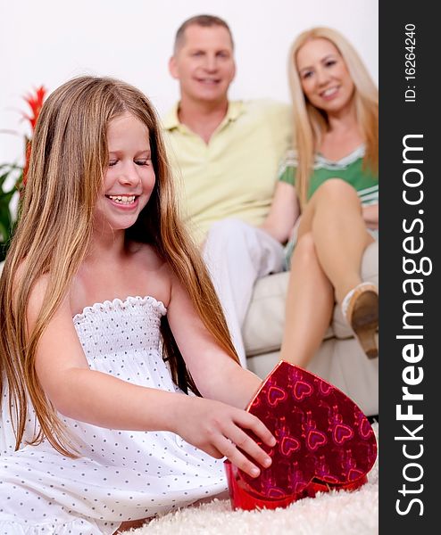 Happy young girl opening a gift box with her parents in living room