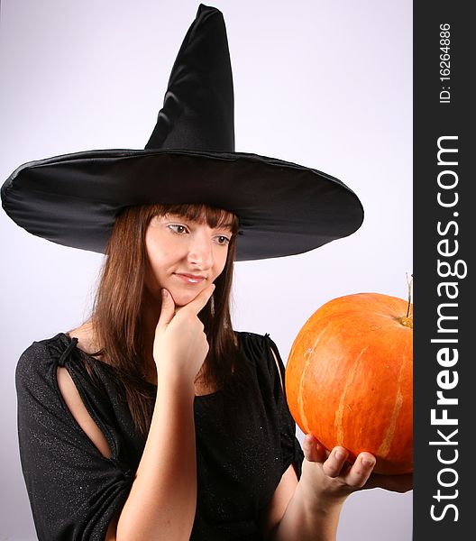 Young witch contemplating over a pumpkin. Young witch contemplating over a pumpkin