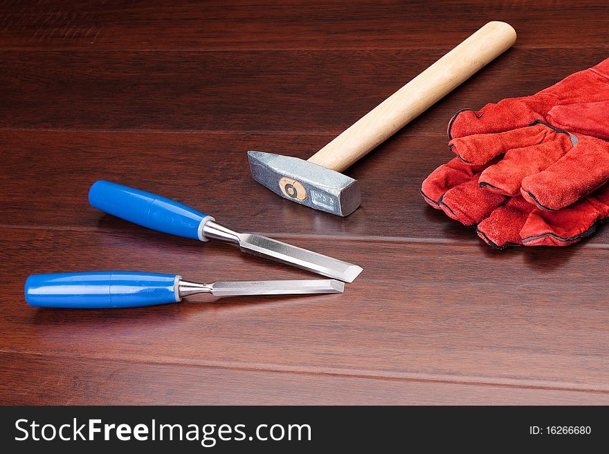 Red gloves, hammer and blue chisels on dark background. Red gloves, hammer and blue chisels on dark background