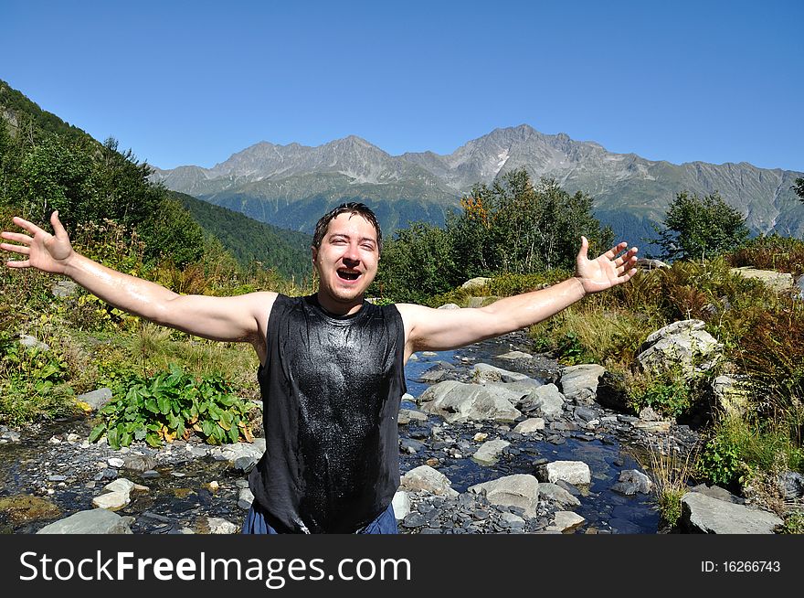The young man threw up his arms to the side, the background a mountain river, mountain top