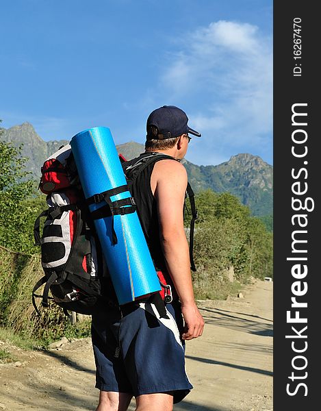 Tourist with a large backpack is a high mountain, on the road, photo from the back