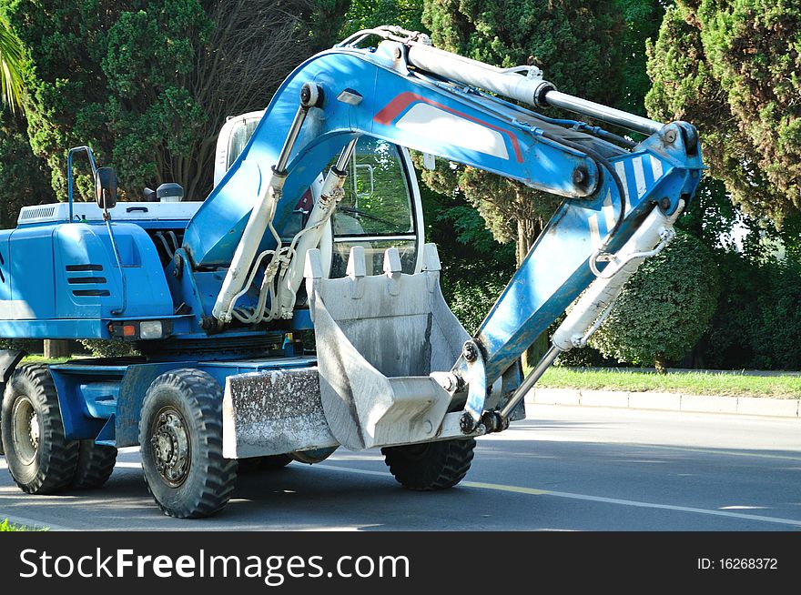 Large, blue excavator driving on the highway, front view