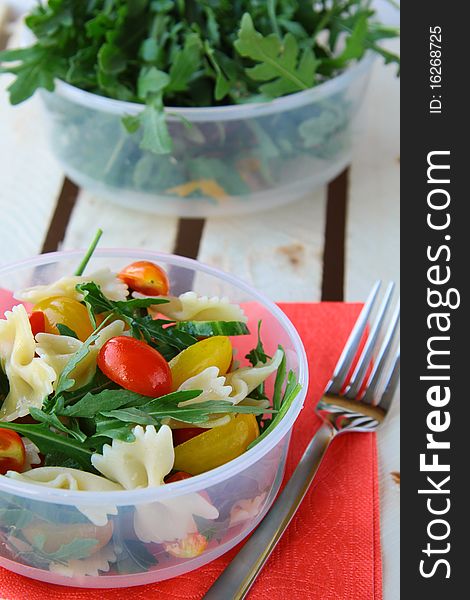 Salad with tomatoes and arugula and pasta in a glass bowl