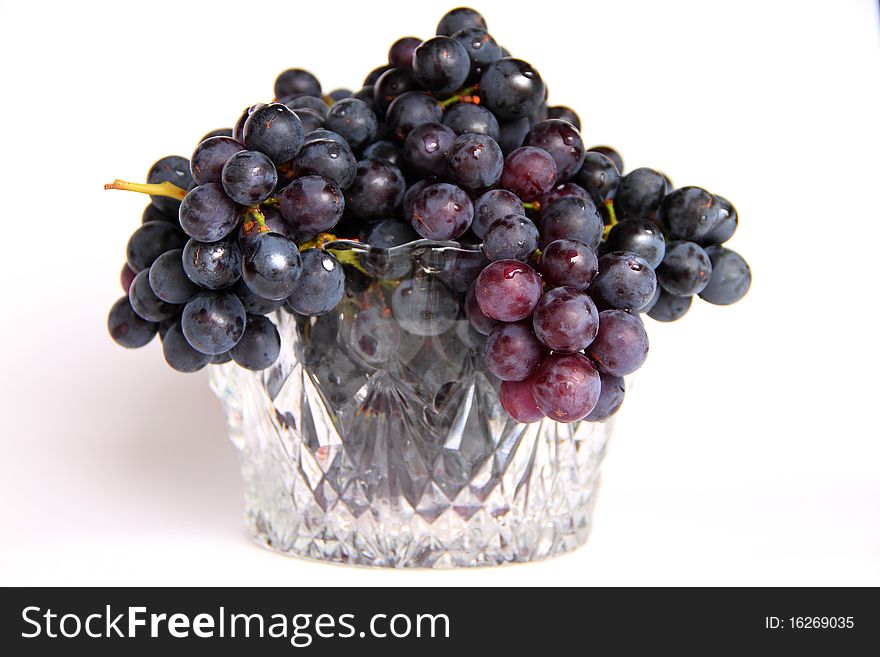 Black grapes in a crystal vase on a white background