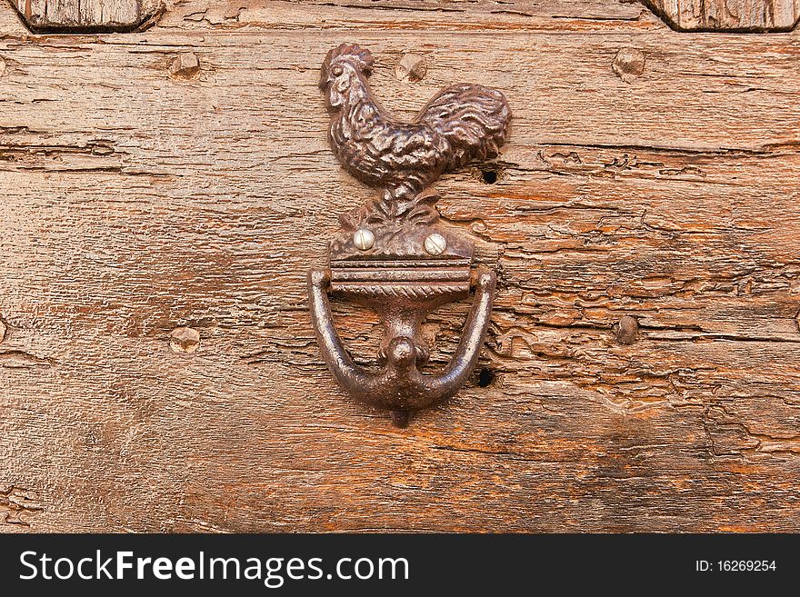 Metal cock as doorknocker on wooden background