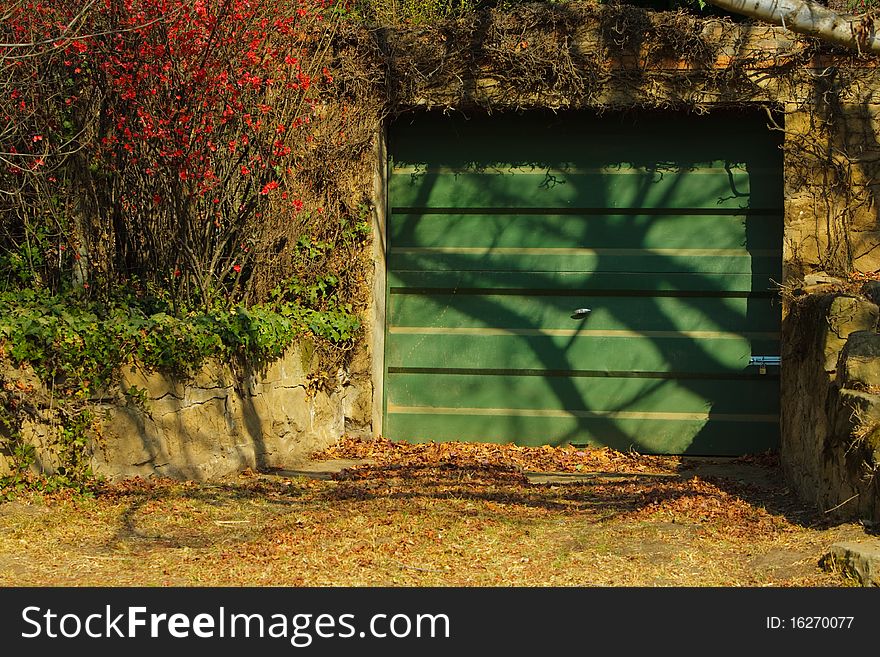 A modern green steel garage door in an old stone wall covered in autumn foliage. A modern green steel garage door in an old stone wall covered in autumn foliage.