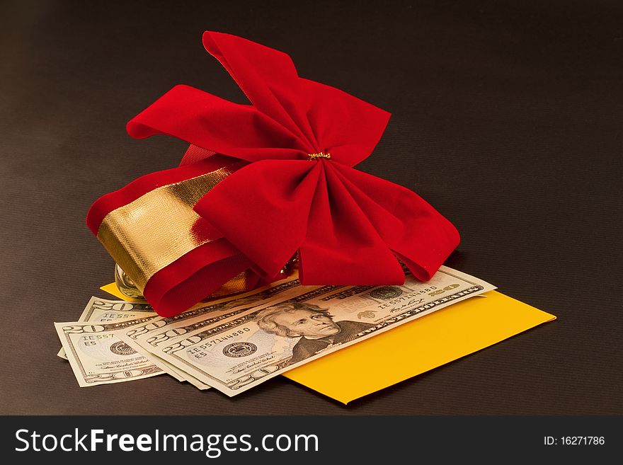 Holiday cash gift of dollars, especially in difficult times, is in yellow envelope with red velvet bow accent against black background. Holiday cash gift of dollars, especially in difficult times, is in yellow envelope with red velvet bow accent against black background