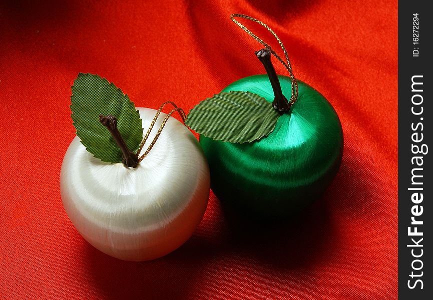 Two apple decorations on a red silk background. Two apple decorations on a red silk background