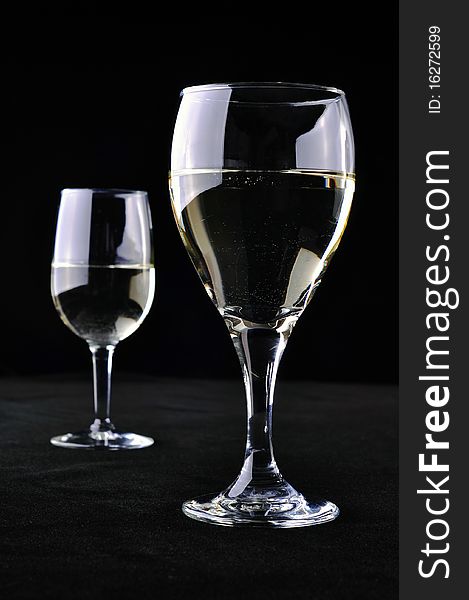Two glasses of white wine, separated from each other, on a black background