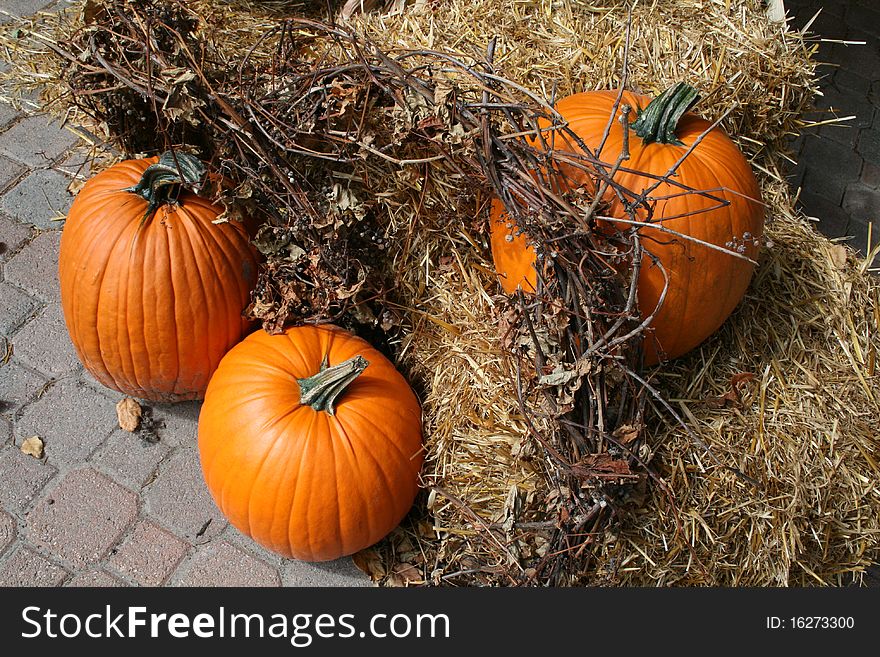 Three yellow pumpkins with straw on the floor