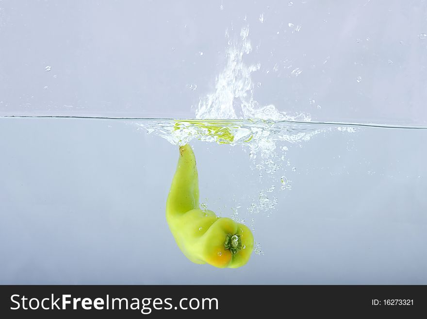 Green chilli thrown in water with gray background