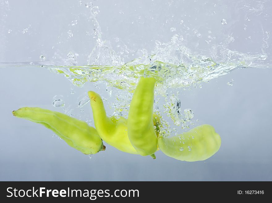 Green chilli thrown in water with gray background