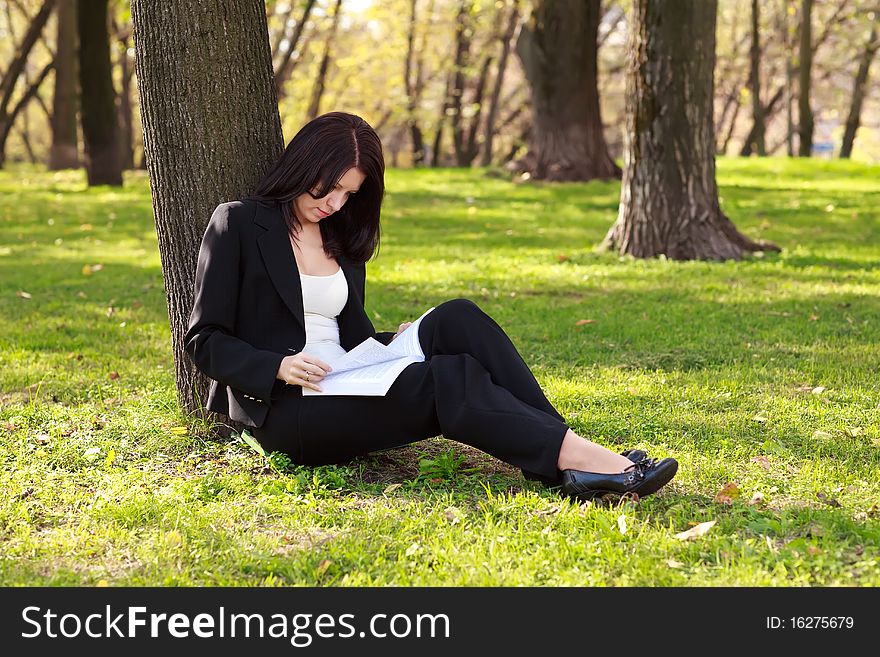 Young businesswoman sitting on the grass and reading book outdoor. Young businesswoman sitting on the grass and reading book outdoor