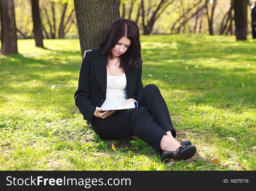 Young businesswoman sitting on the grass and reading book outdoor. Young businesswoman sitting on the grass and reading book outdoor