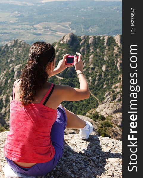 Girl sits on rocky edge and photographs a landscape. Girl sits on rocky edge and photographs a landscape