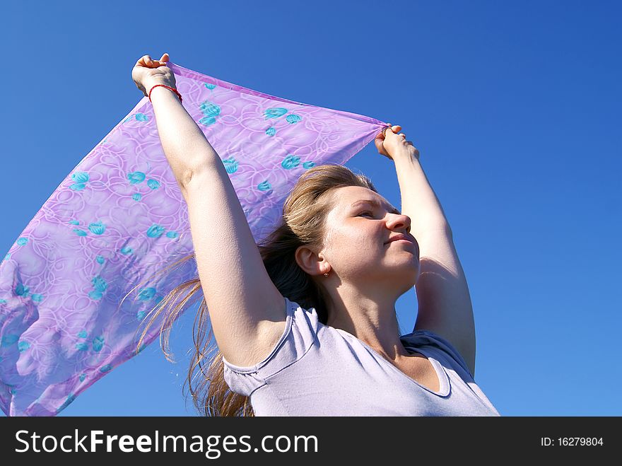The woman holds in hands over a head a female scarf against the dark blue sky. The woman holds in hands over a head a female scarf against the dark blue sky