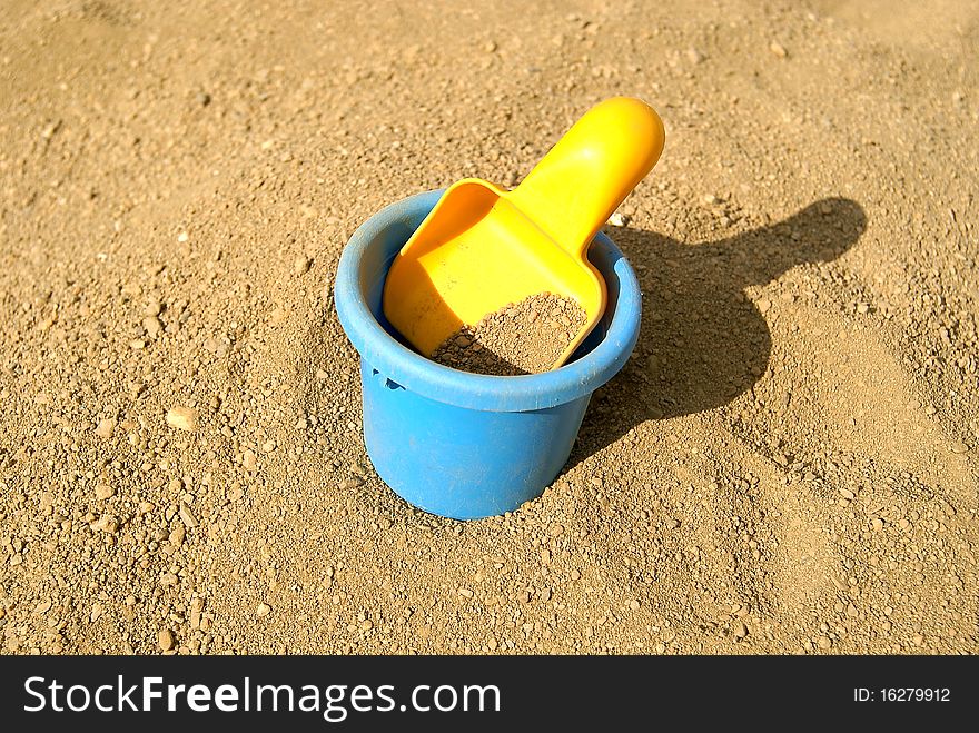 The children's yellow scoop lays in a bucket with sand. The children's yellow scoop lays in a bucket with sand