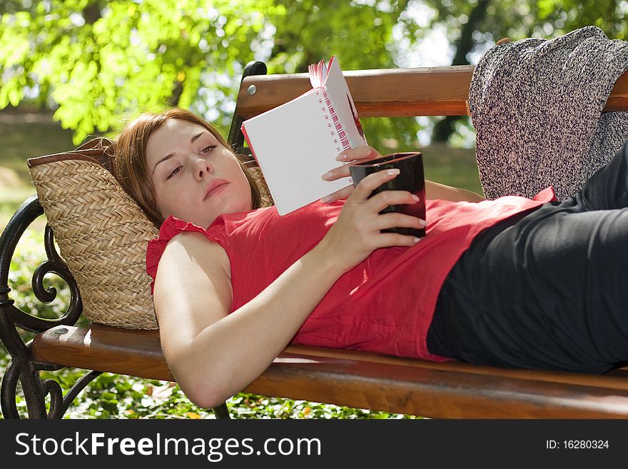 Woman laying on bench with coffee and reading. Woman laying on bench with coffee and reading