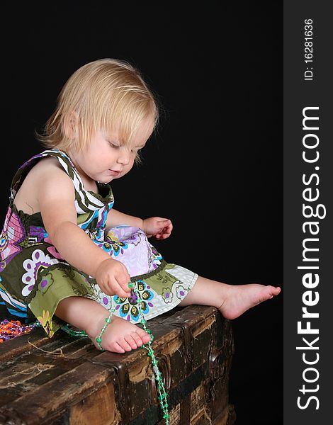 Beautiful blond toddler sitting on an antique trunk playing with beads. Beautiful blond toddler sitting on an antique trunk playing with beads