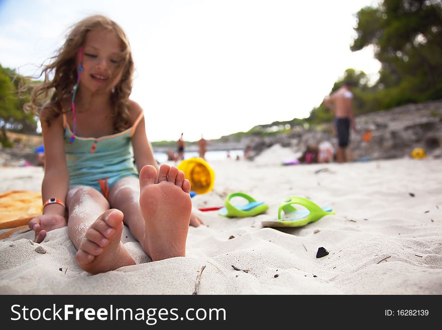 Sute little girl sits at the beach with her toys. focus on foots. Sute little girl sits at the beach with her toys. focus on foots.