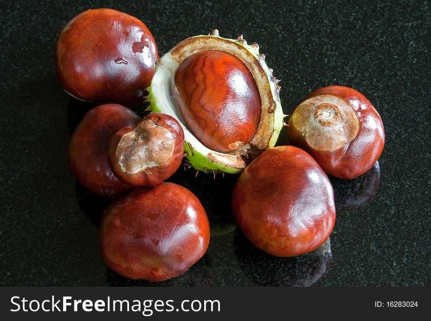 A collection of gleaming conkers against a black granite background