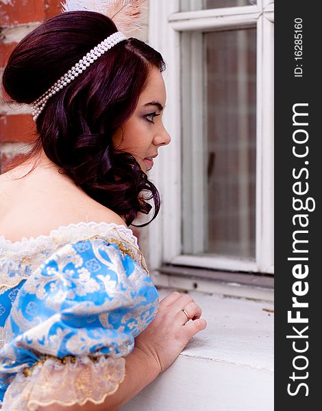 A portrait of lady in a blue baroque dress looking out a window. A portrait of lady in a blue baroque dress looking out a window