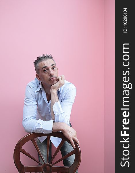 Man with blue shirt leaning on a wooden chair. Man with blue shirt leaning on a wooden chair