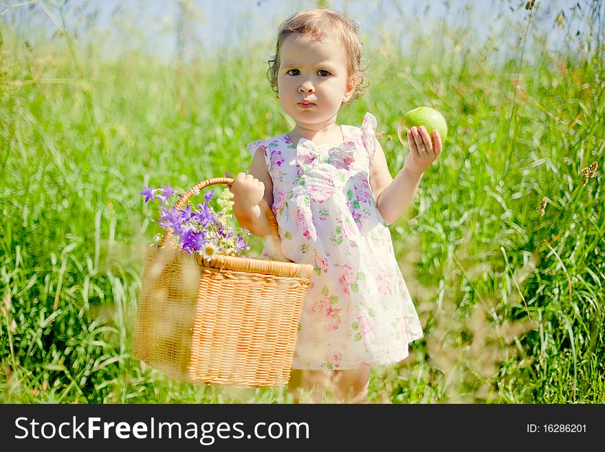Little beautiful girl holding picnic basket in one hand and green apple in another one. Little beautiful girl holding picnic basket in one hand and green apple in another one