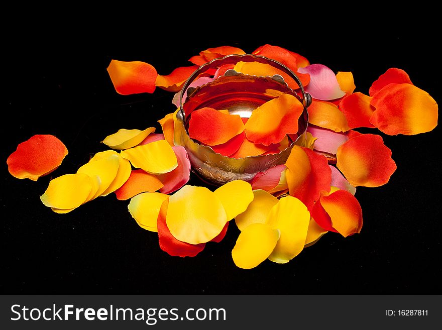 A silver basket on orange, yellow and pink rose textile petals on black. A silver basket on orange, yellow and pink rose textile petals on black