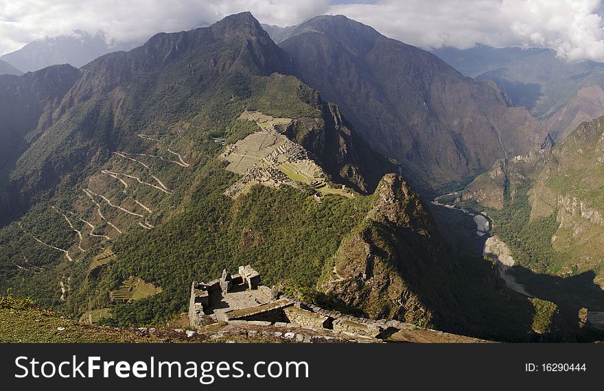 Machu Picchu and mountains seen from some old ruins at Wayna Picchu mountain. View of the winding road coming from Águas Calientes. Slight mist.