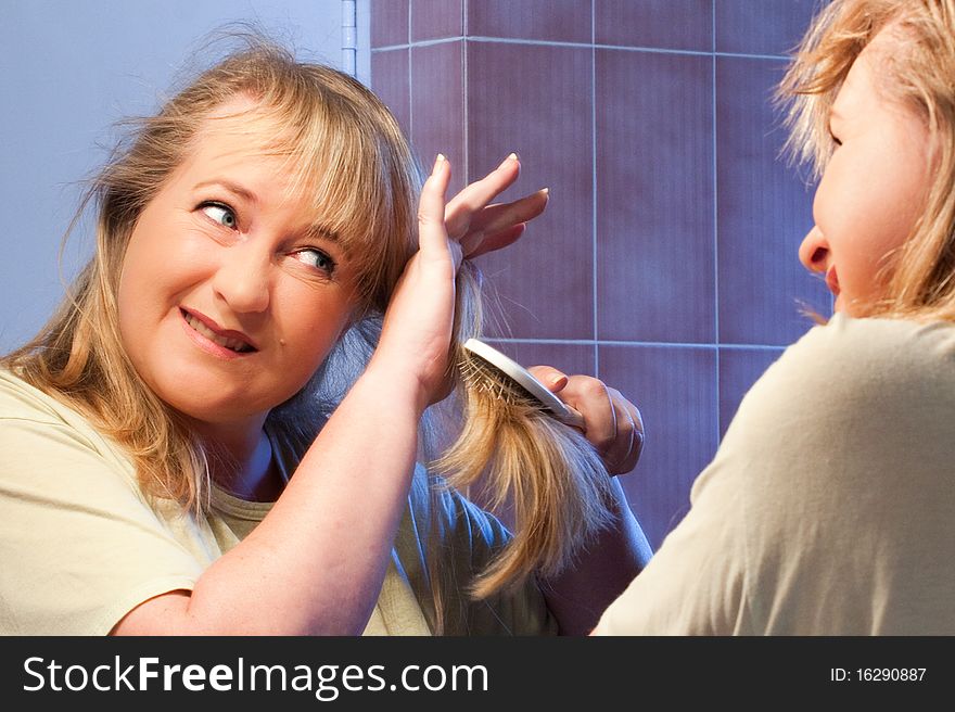 Mature caucasian woman struggling to brush out her tangled hair in mirror. Mature caucasian woman struggling to brush out her tangled hair in mirror