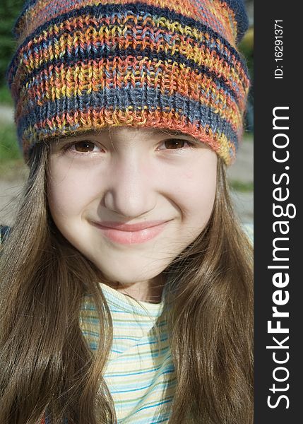 Closeup cute smiling girl in colored knitted hat with long brown hair